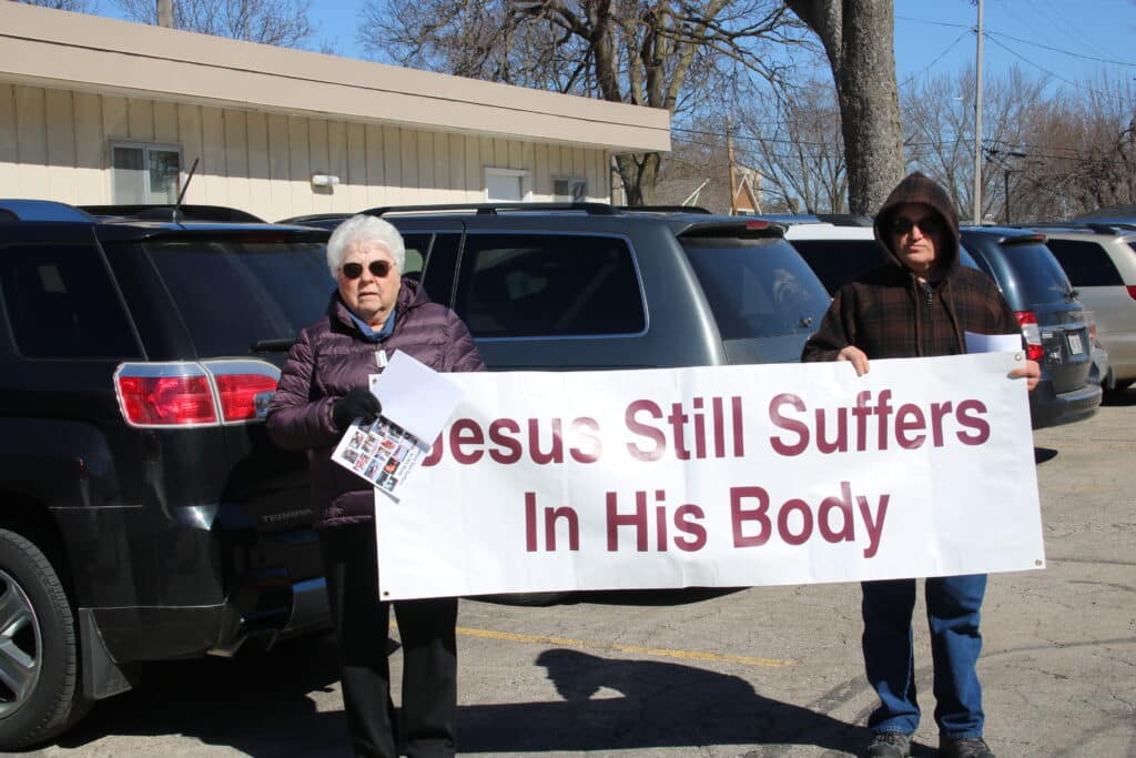 Franciscan Sister of Perpetual Adoration Marlene Weisenbeck and FSPA affiliate Raymond List carry the banner "Jesus Still Suffers In His Body" during a Justice and Peace Way of the Cross Good Friday walk in La Crosse, Wisconsin.