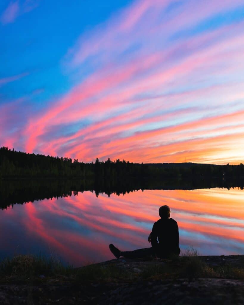 Silhouette of man sitting in front of lake and shoreline with a colorful sky