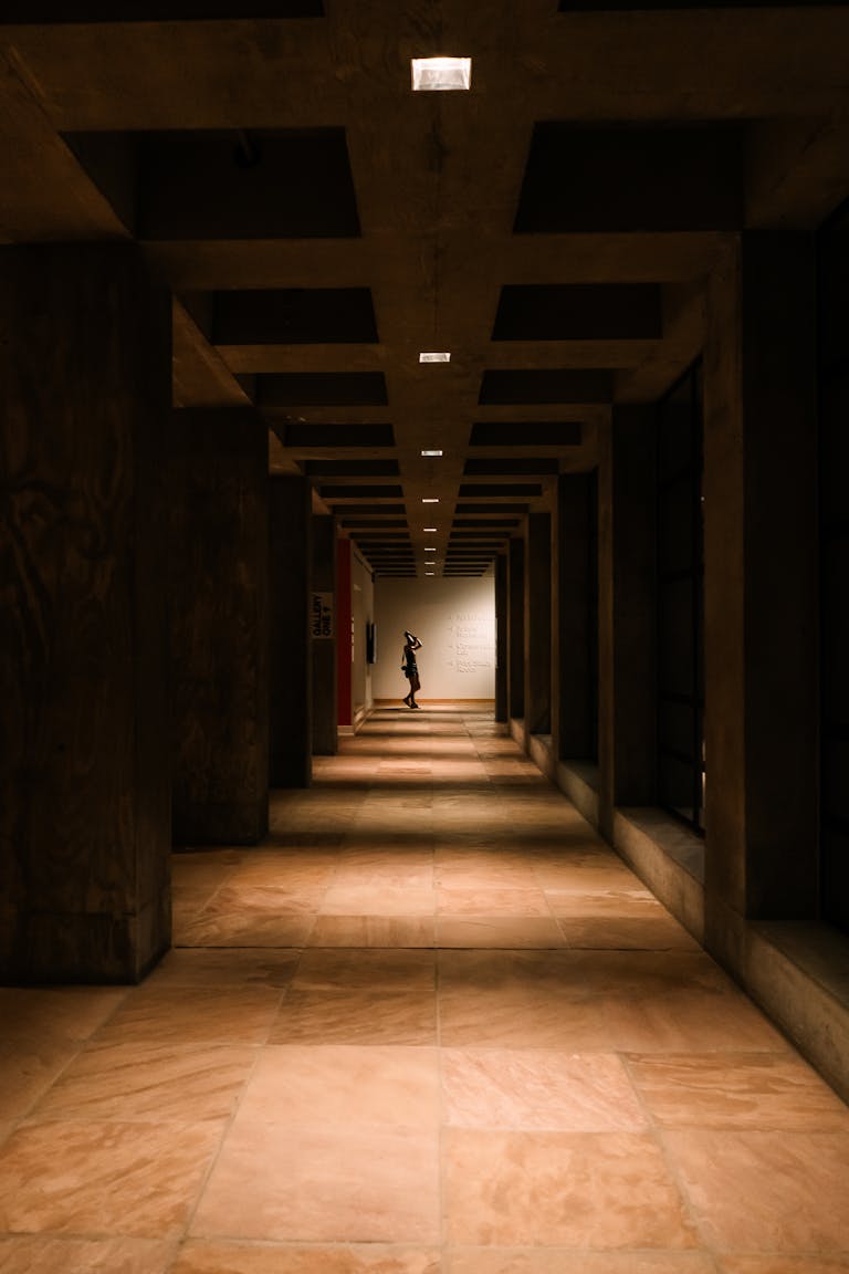 A moody, dimly lit corridor with a solitary figure standing at the end, Tempe, AZ.