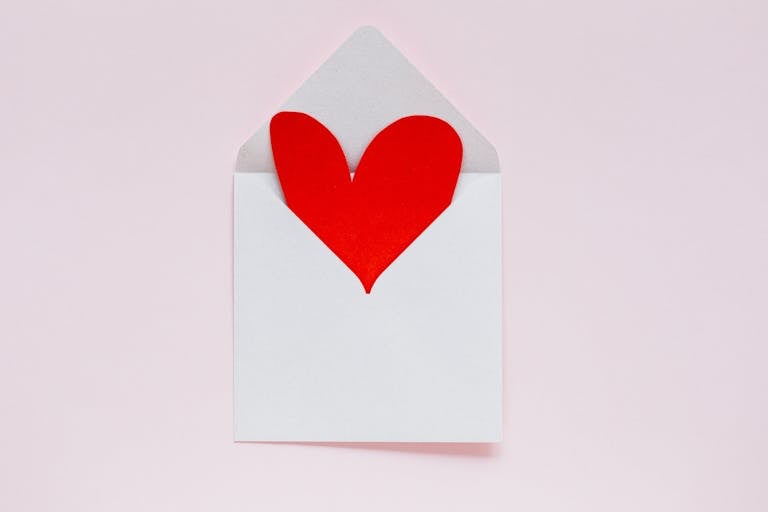 A red heart paper cutout in an envelope on a pastel pink background, ideal for Valentine themes.