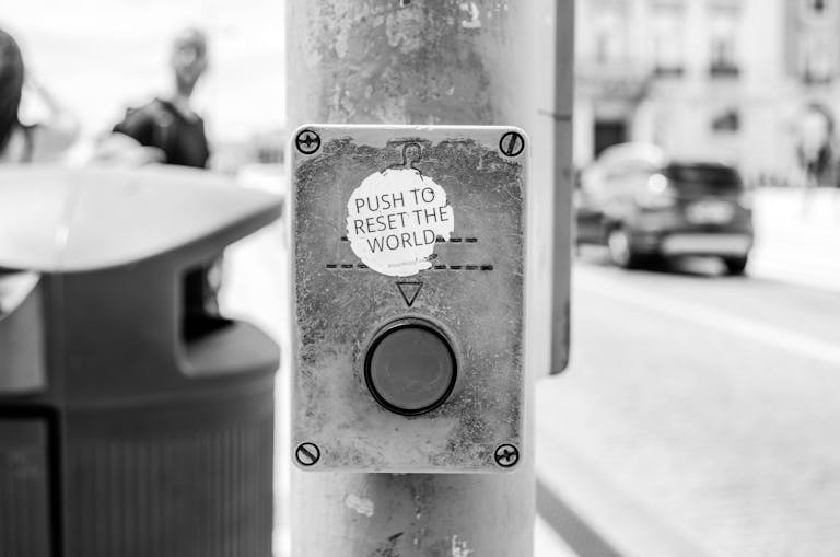 Grayscale photo of a street button labeled 'Push to reset the world', Lisbon urban scene.